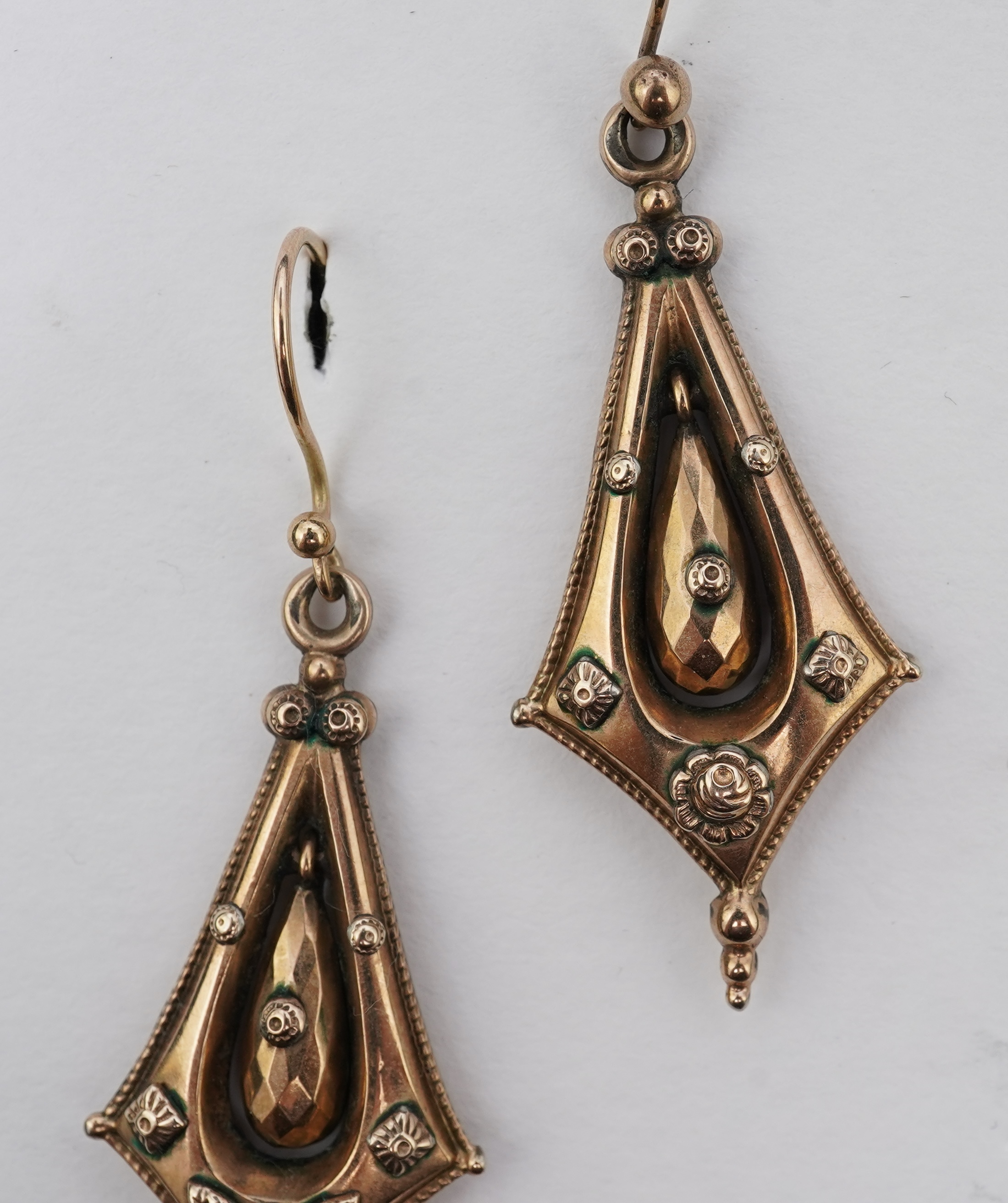 A pair of Victorian gold earrings, late 19th century, each of drop design, outlined with a rope twist border and accented with floral and foliate motifs, the centres suspending faceted pendants, length 5.8cm, one slightl